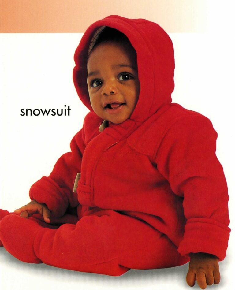 A baby wearing a red snowsuit and hood sits on a white background, smiling at the camera.